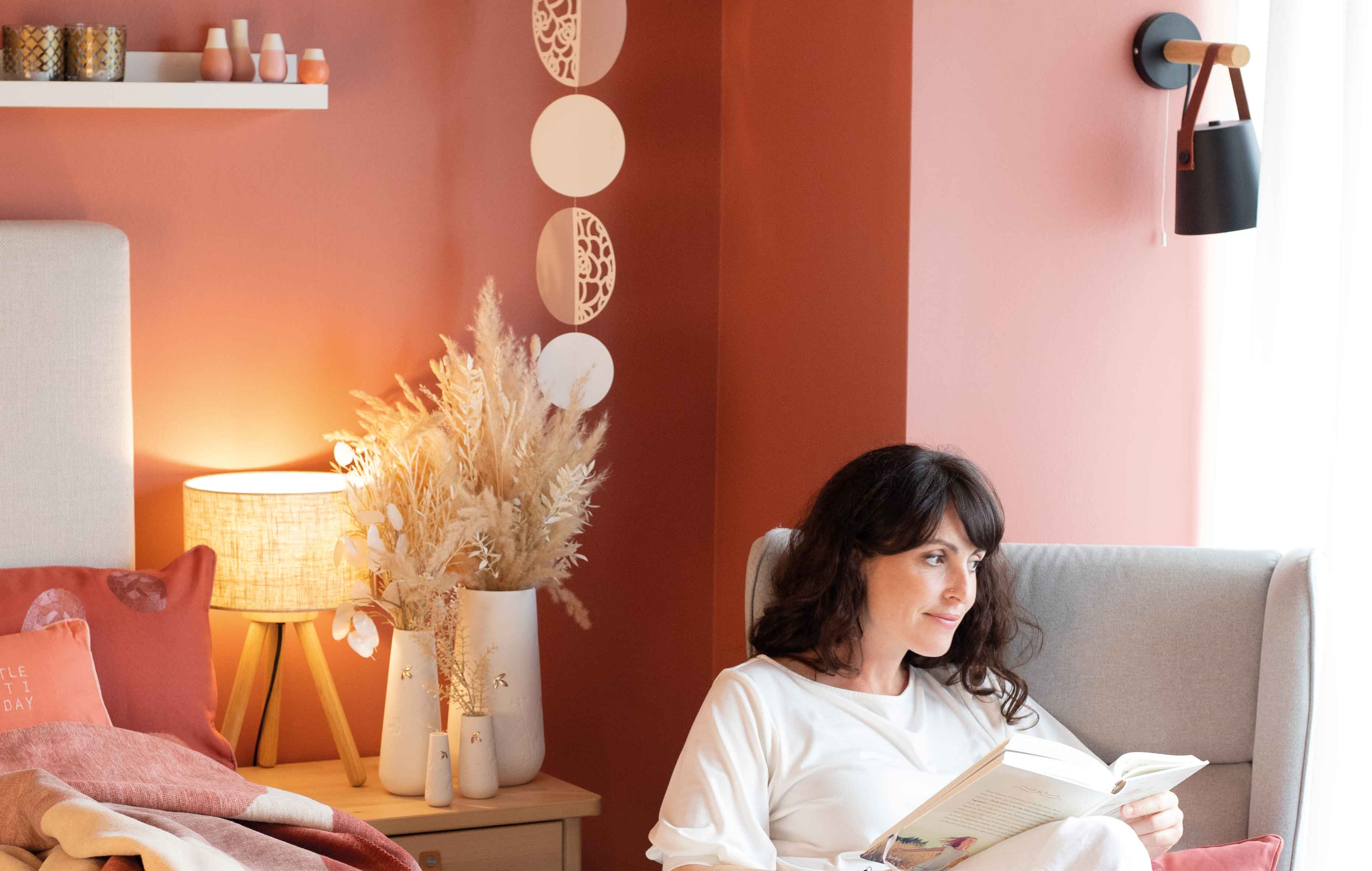 Das Foto zeigt eine Frau die in liebevoll dekorierter Umgebung ein Buch liest.
